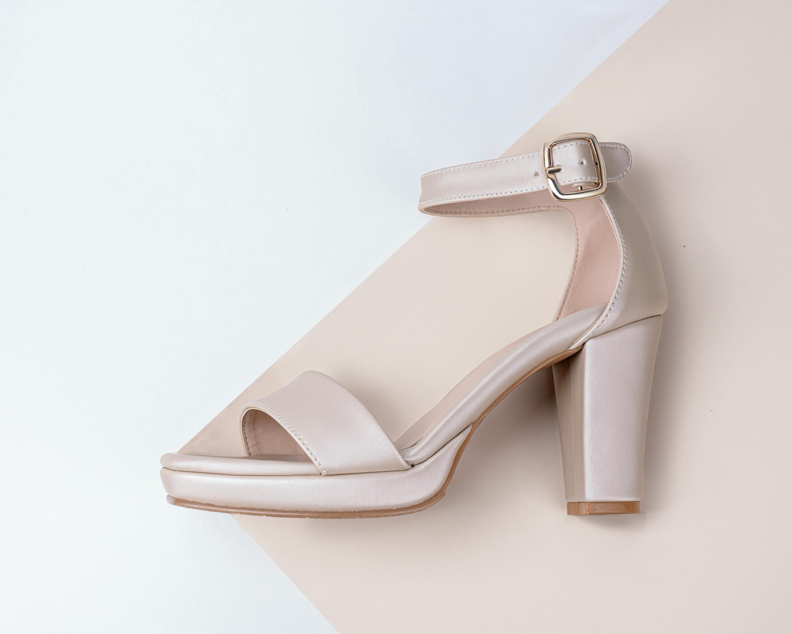 Stylish beige high-heeled sandal with buckle on an abstract white and beige background.