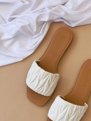 Stylish white quilted slippers on a beige background with white cloth accent.